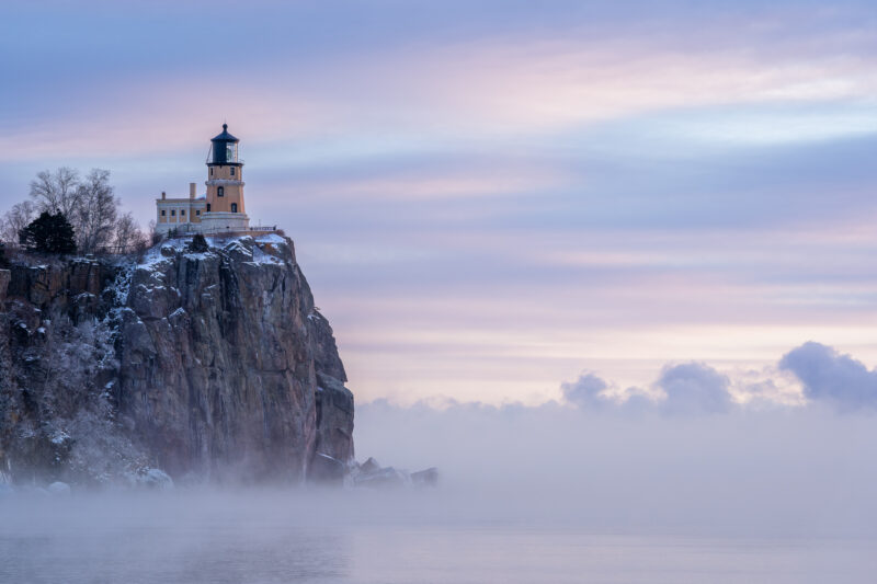 image of a lighthouse on a rock cliff overlooking a lake at sunrise