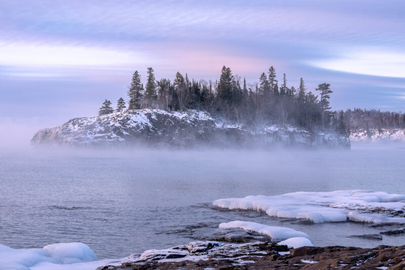 image of sea smoke rising off the water in front of an island